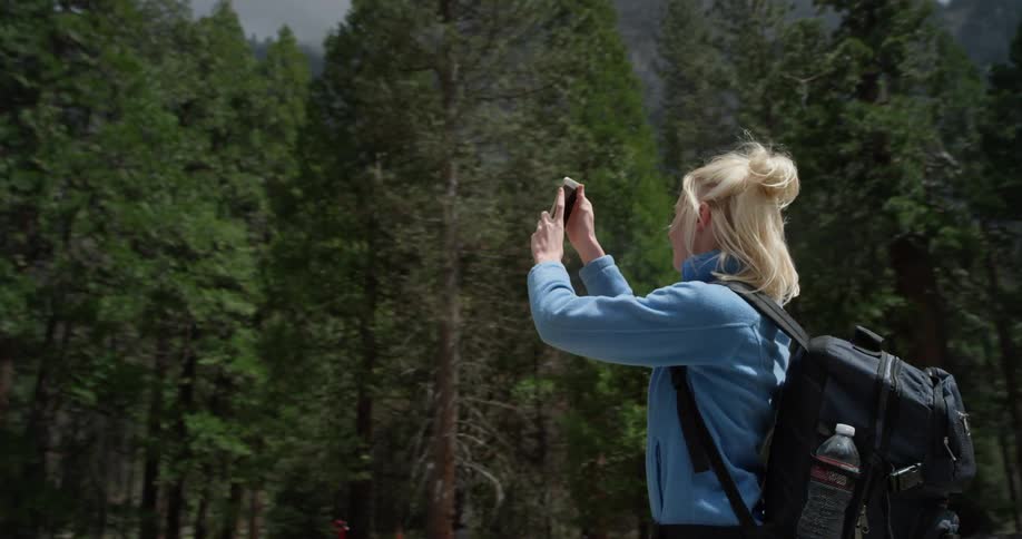 Woman wearing a backpack takes a picture of nature on her phone