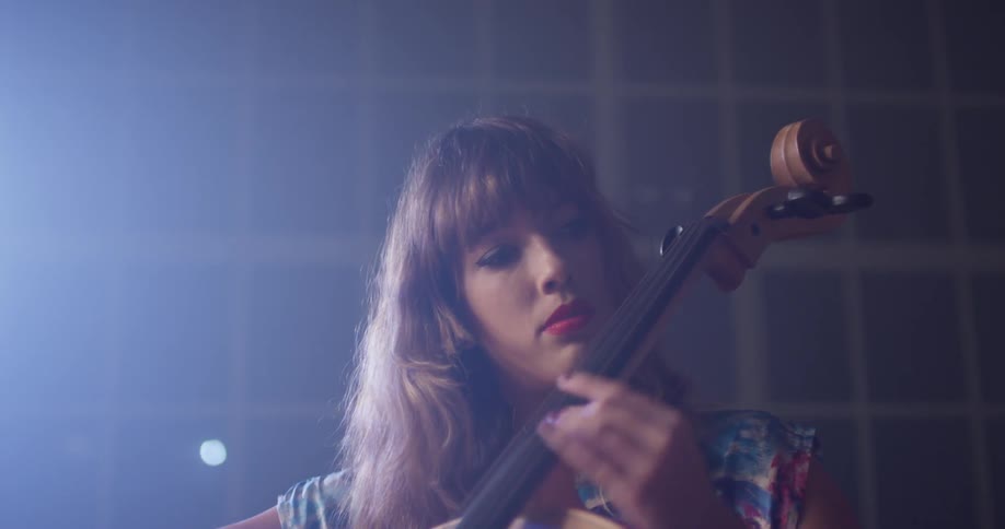 Woman plays cello in a room with a large window at night