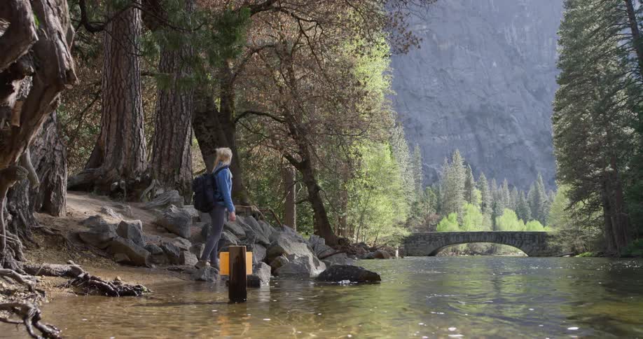 Woman stands at the edge of a stream looking up