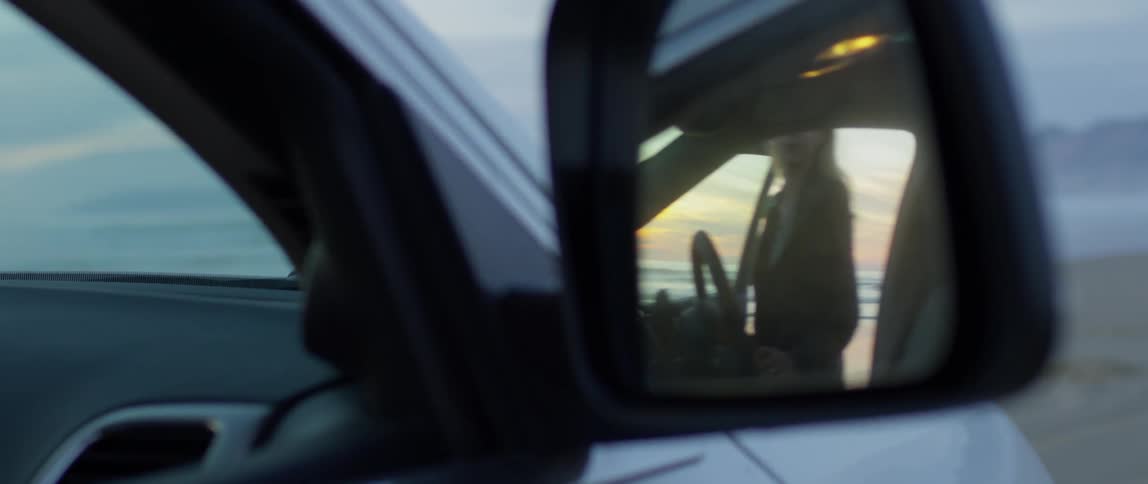 A woman climbs into a car at sunset