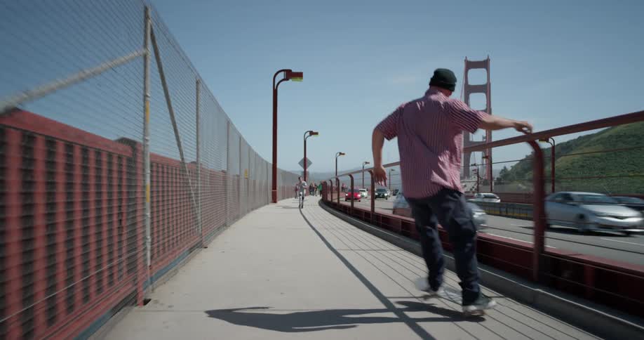 A man is skateboarding on a path across the golden gate bridge on a sunny day