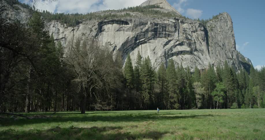Person walks in a large grassy field next to a large mountain