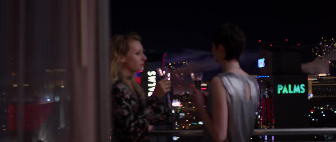 Two women toast on the balcony as fireworks go off
