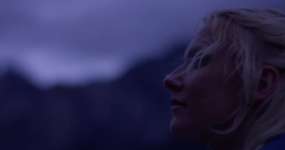A blond haired woman looks out towards the mountains