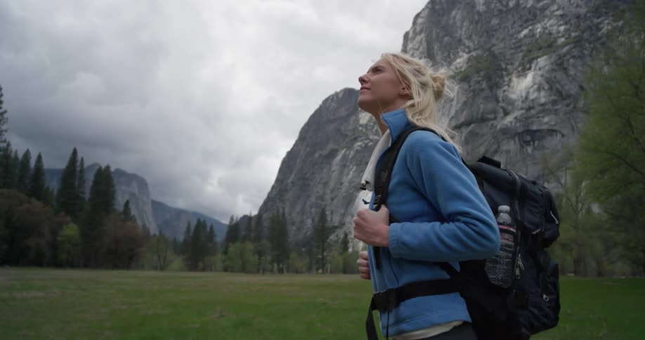 Woman walks in a large grassy field near a tall mountain