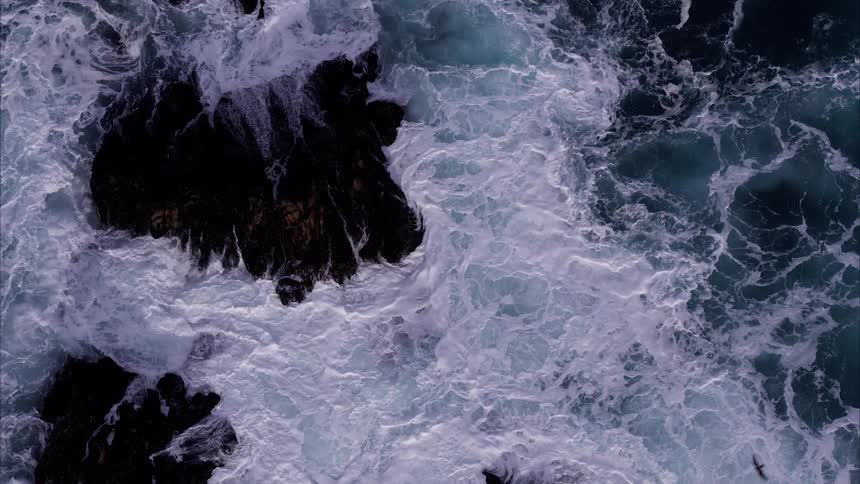 Ocean waves flow around large rocks and crash over them
