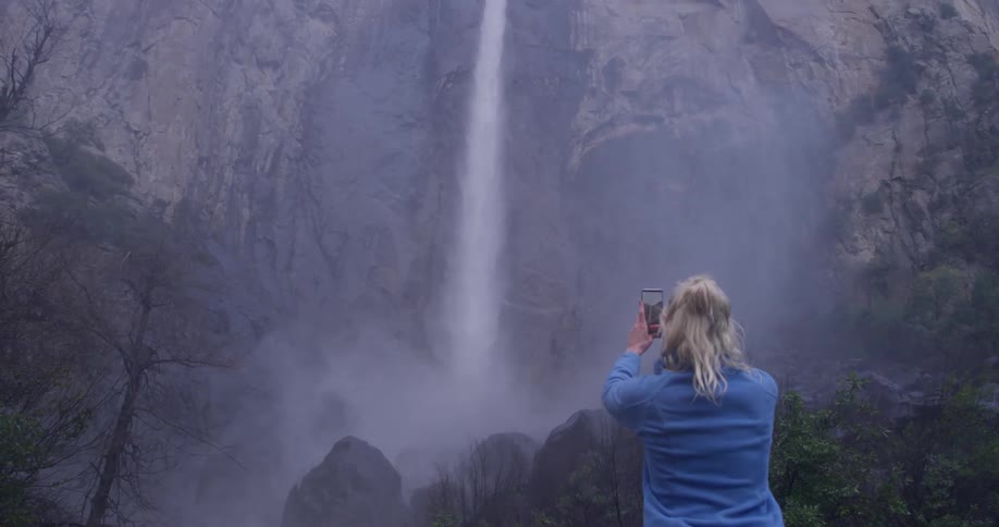 A woman photographs a waterfall in mountains