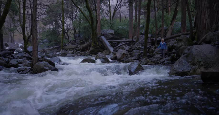 Woman walks on a rocky area next to a stream