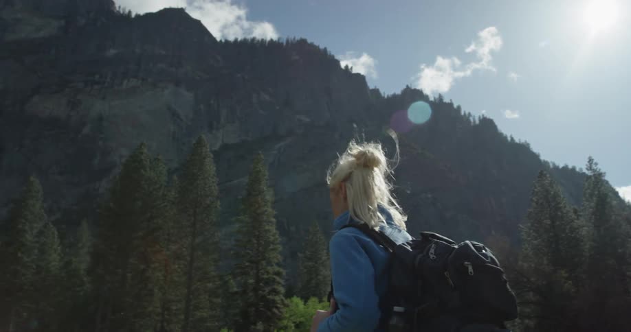 A woman carries a backpack as she hikes near the mountains