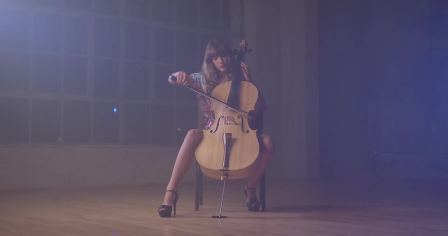 A woman plays a cello in a dim room
