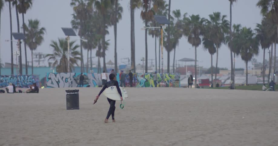 A surfer carries a surfboard on a beach