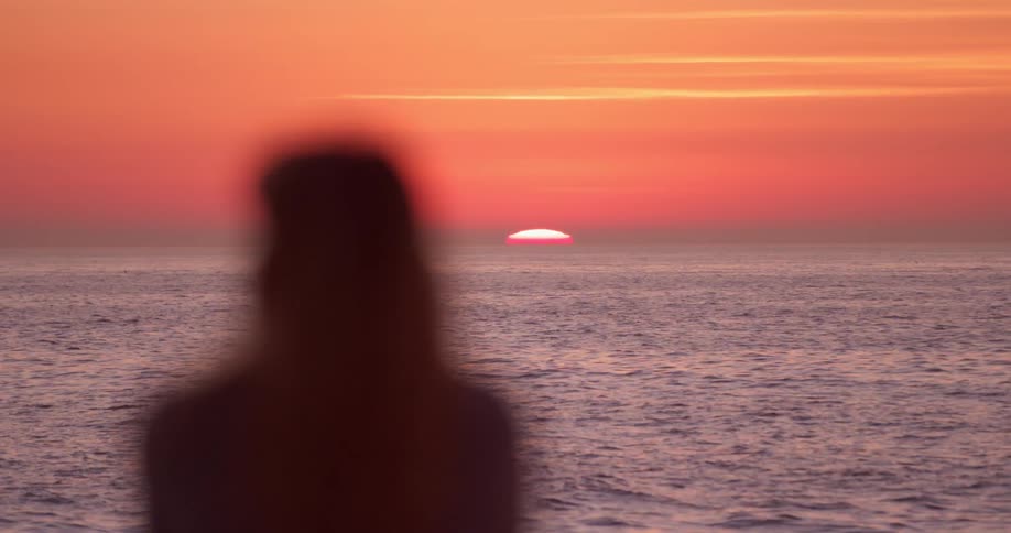 Woman stands on the beach at sunset looking over