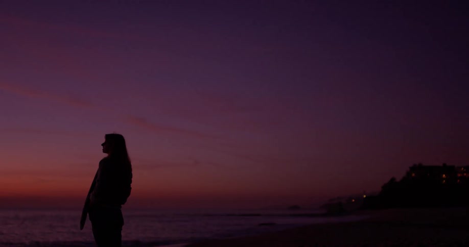 Woman stands outside on the beach at sunset