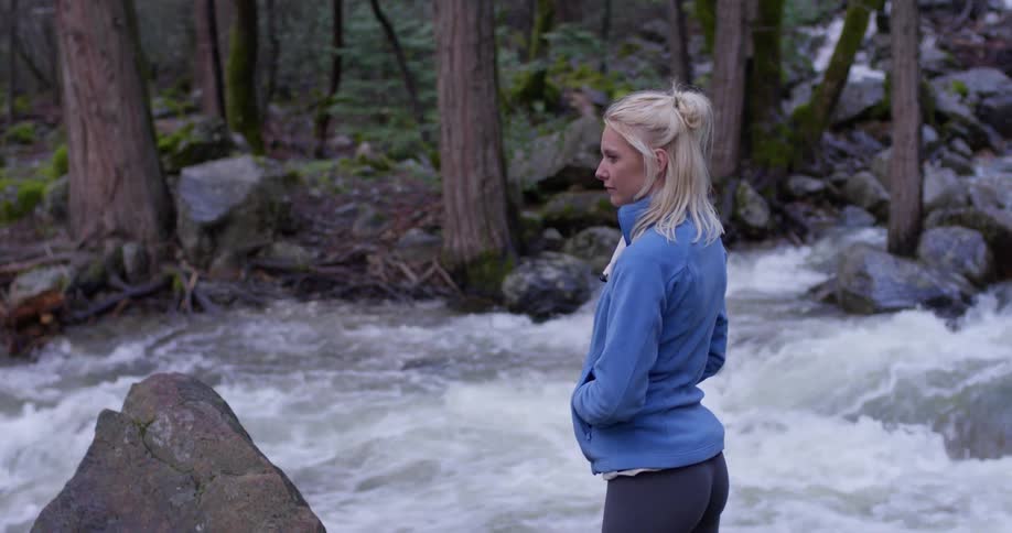 A woman stands next to a river in a forest