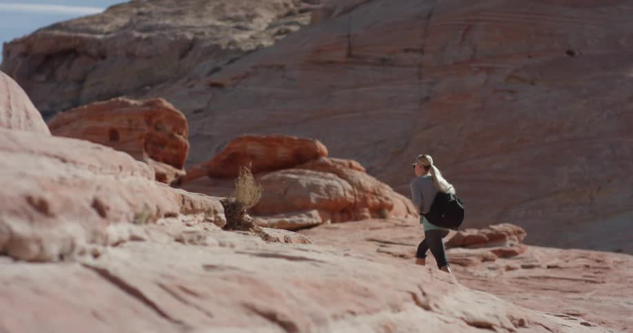 Woman walks on rocky hilly terrain on a sunny day