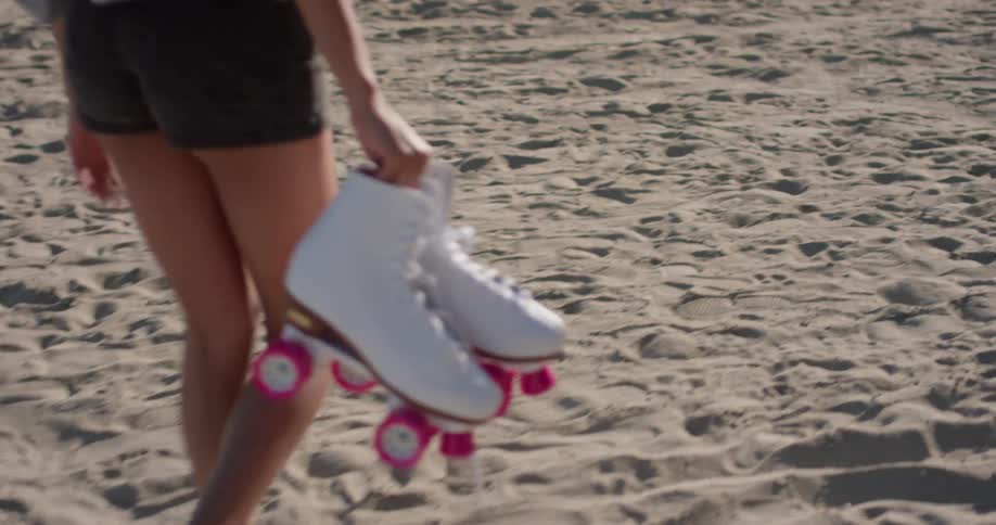 A woman carries roller skates on the beach