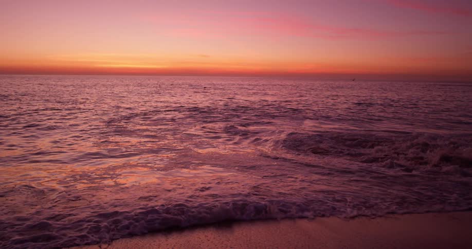 Ocean waves wash onto a beach at sunset