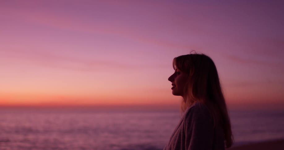 Woman with long hair looks out at the ocean at sunset