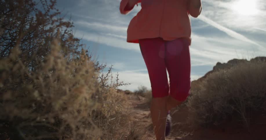 Woman jogs on a dirt path through the bushes on a sunny day