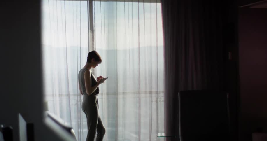 Woman stands next to a large window looking at her phone