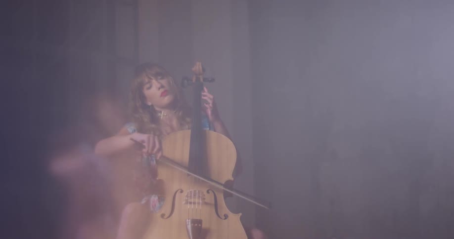 A woman plays a cello in a dim room