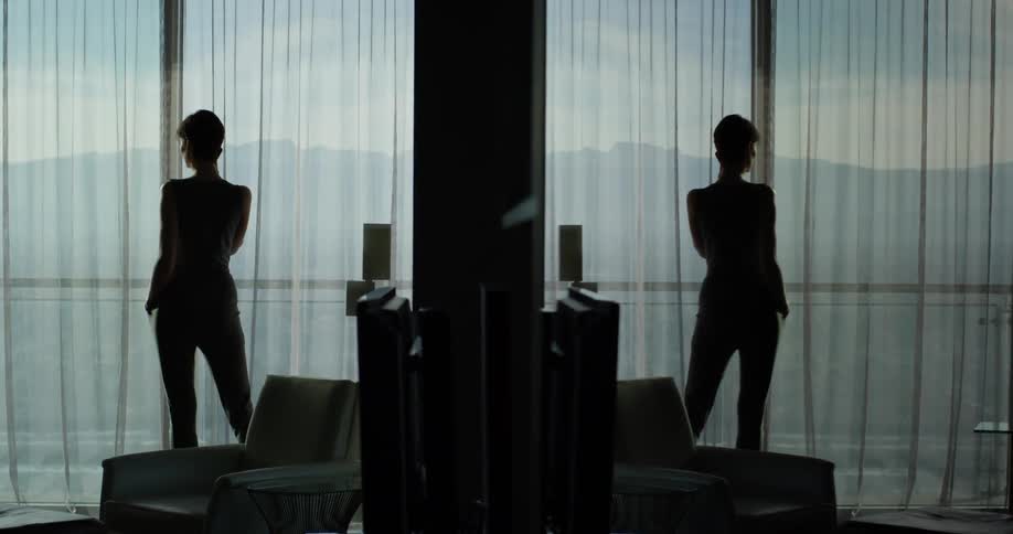 A mirror image of a woman talking on the phone while looking out glass doors