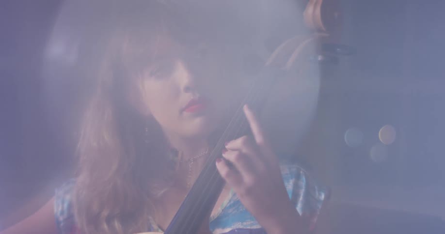 A woman plays a cello in front of windows
