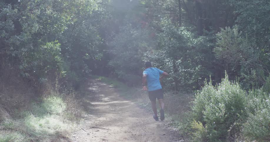 The man jumps and runs downhill in the forest