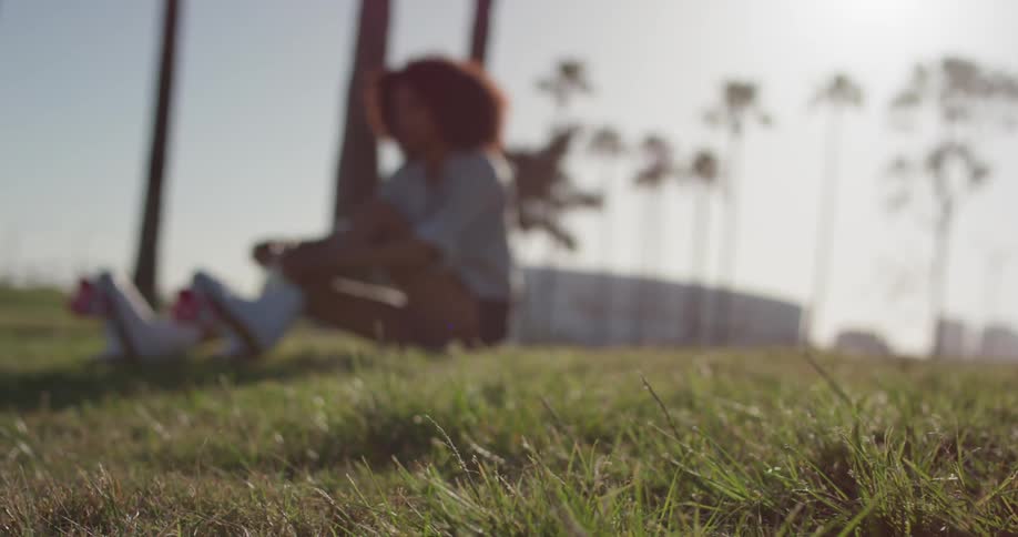 Woman sits in the grass on a sunny day tying her roller skates