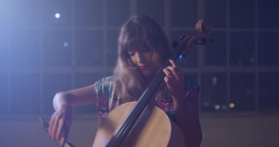 A woman plays a cello in front of windows