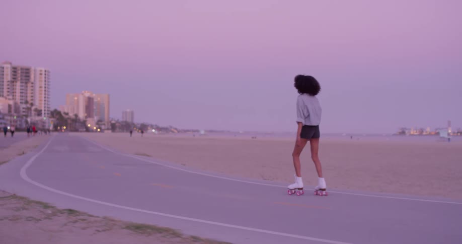 A woman skates on a beach at sunset