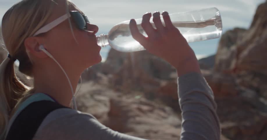 A woman drinks from a bottle of water while looking at rocky terrain