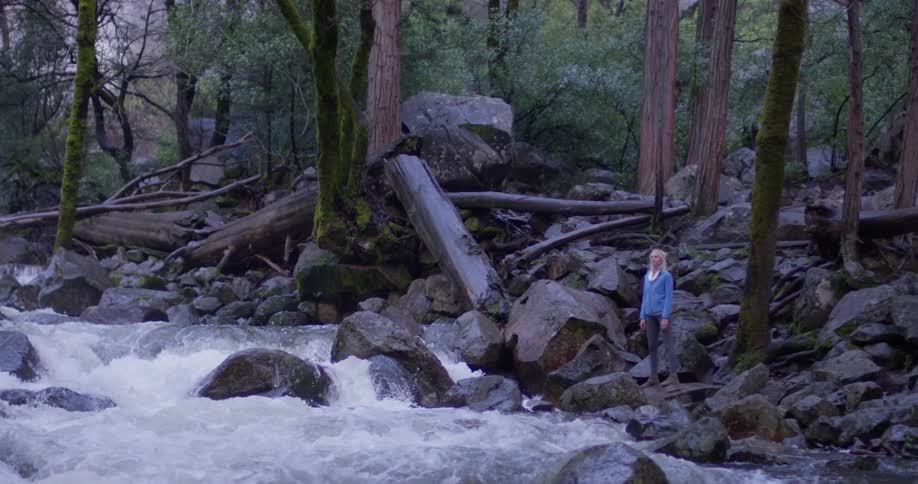 A woman stands on rocks on the side of the river