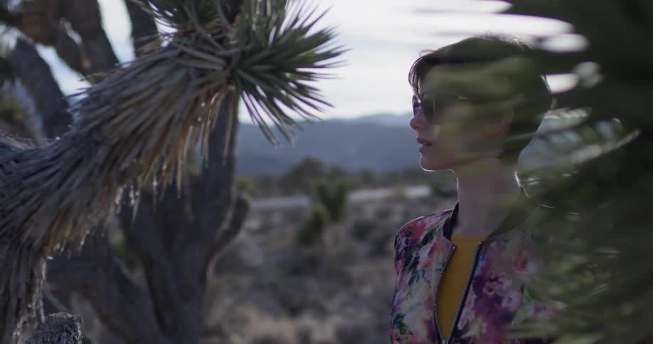 A woman stands next to a plant in a desert