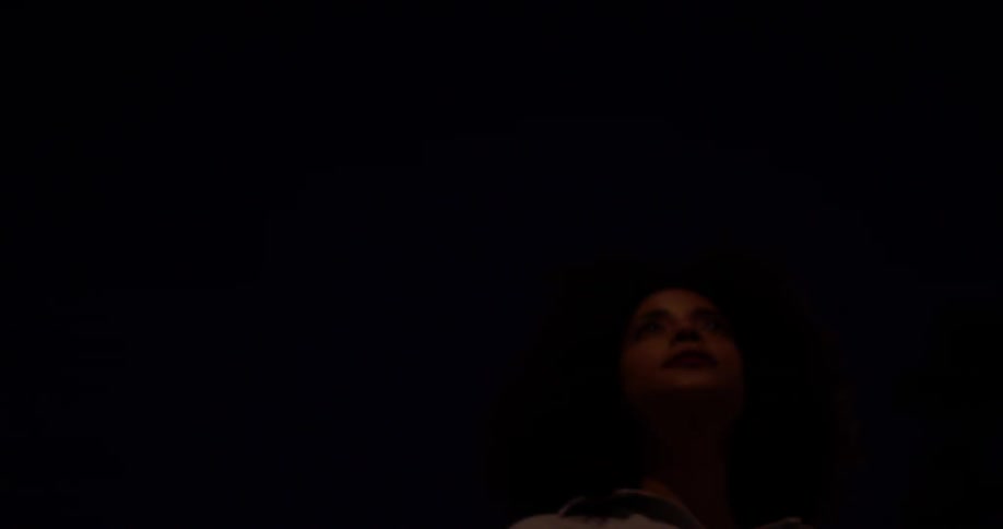 A woman looks up at palm trees and street lights at night