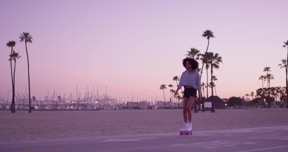 A woman skates on a beach at sunset