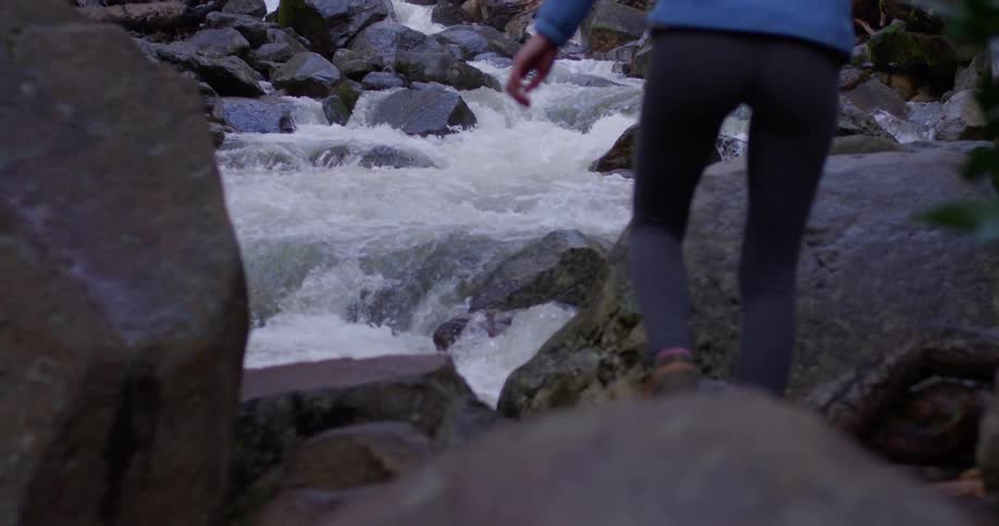 The woman climbs up the rocks by the stream