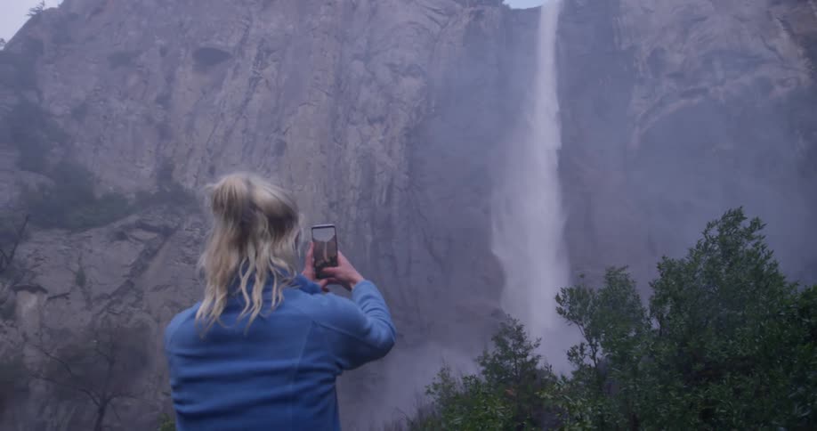 A woman takes a photograph of a waterfall
