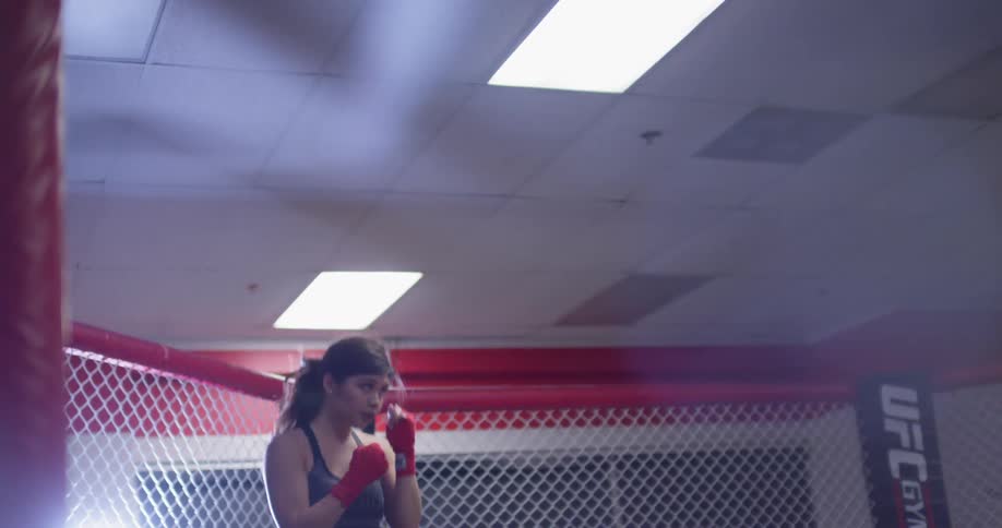 Woman walks into a fenced in area in a gym and practices punching