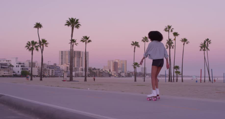 A woman is rollerskating on the beach at sunset
