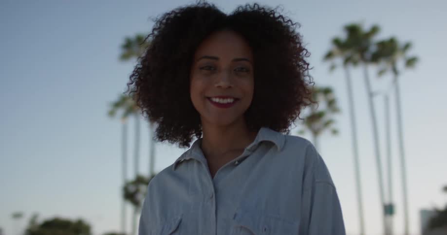 A woman smiles outside near the palm trees