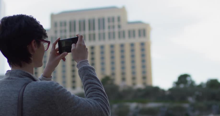 A woman stands outside taking a video of large buildings with her phone
