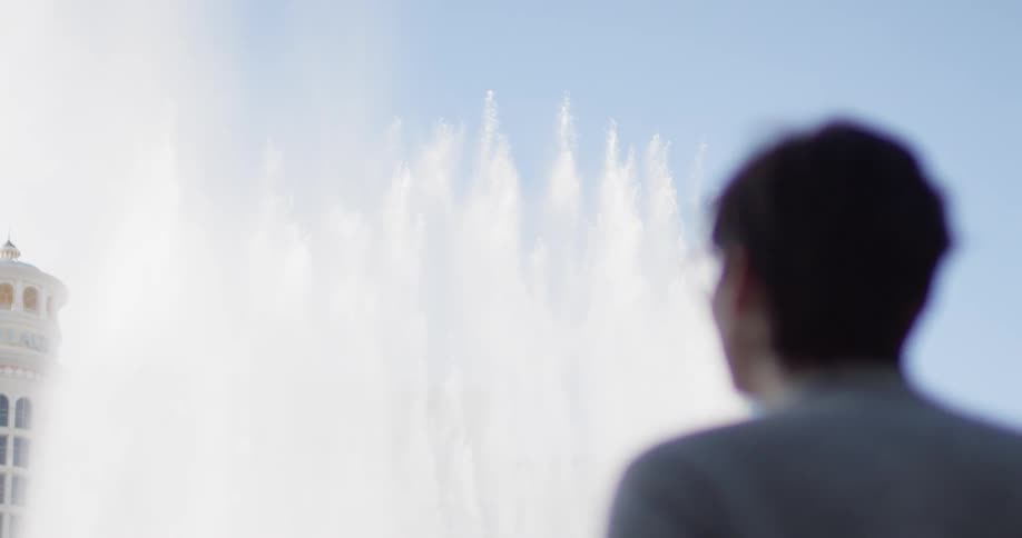 Man watches the water rise from the fountains under a blue sky