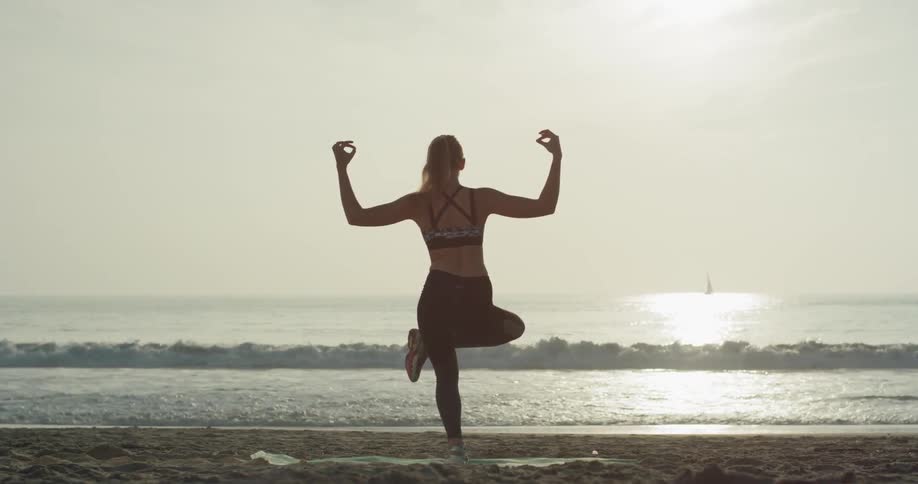 A woman is doing yoga on the beach at sunset