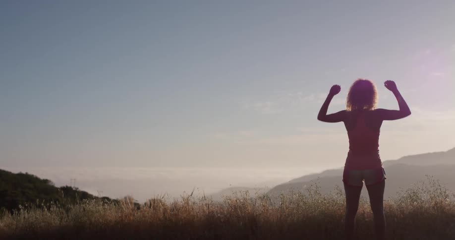 A woman stretches on the hills at sunset