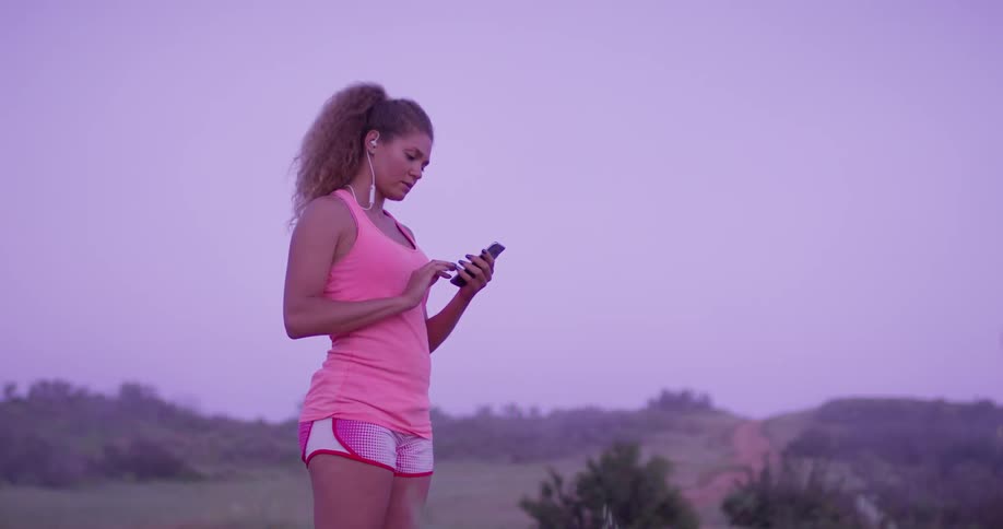 Woman wearing earphones walks outside and stops to look at her phone
