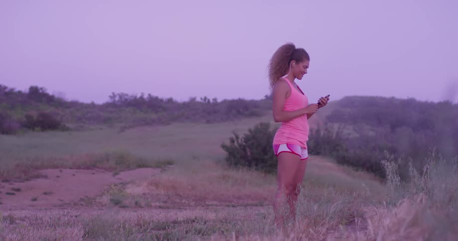 Woman stands in nature looking at her phone and smiling