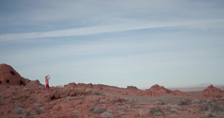 A woman is taking a drink from a water bottle as she stands in the desert