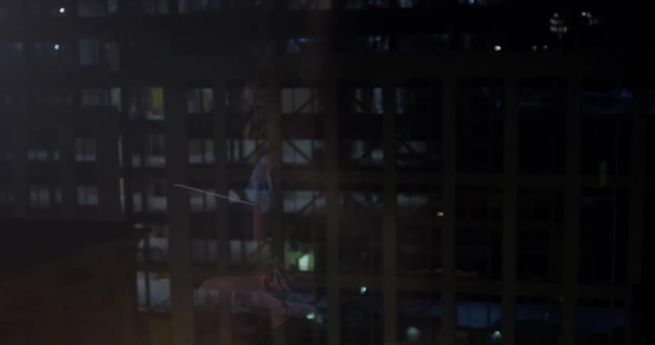 A woman sitting down to play the cello is reflected in the window glass