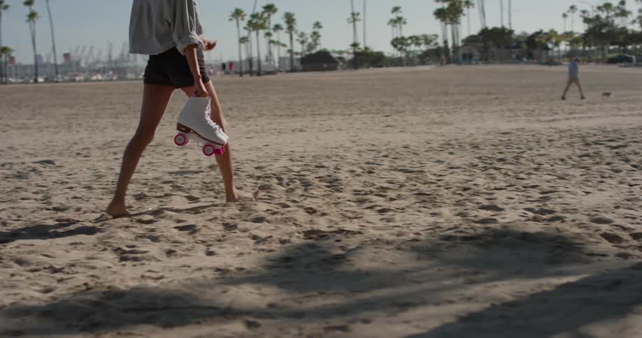 A woman carries roller skates on the beach